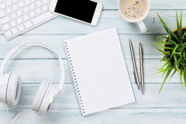 Notepad, headphones, phone and pc on wooden desk table. Top view with copy space