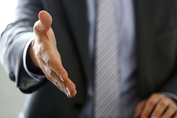 Man in suit and tie give hand as hello in office