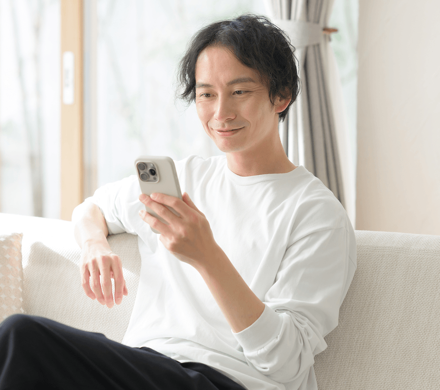 ソファに座ってスマートフォンを見る男性